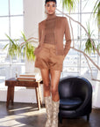 Woman wearing faux suede modern shorts with matching cardigan and snakeskin boots in a bright room