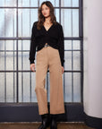 Woman wearing tan Rylee Crop Pants with wide-leg cropped fit and black top standing indoors