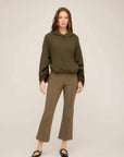Woman wearing olive green Sigourney Pintuck Pants with cropped flare and elastic waistband paired with matching hoodie