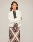 Woman wearing white Cely Cropped Cardigan with long sleeves and open front over patterned skirt