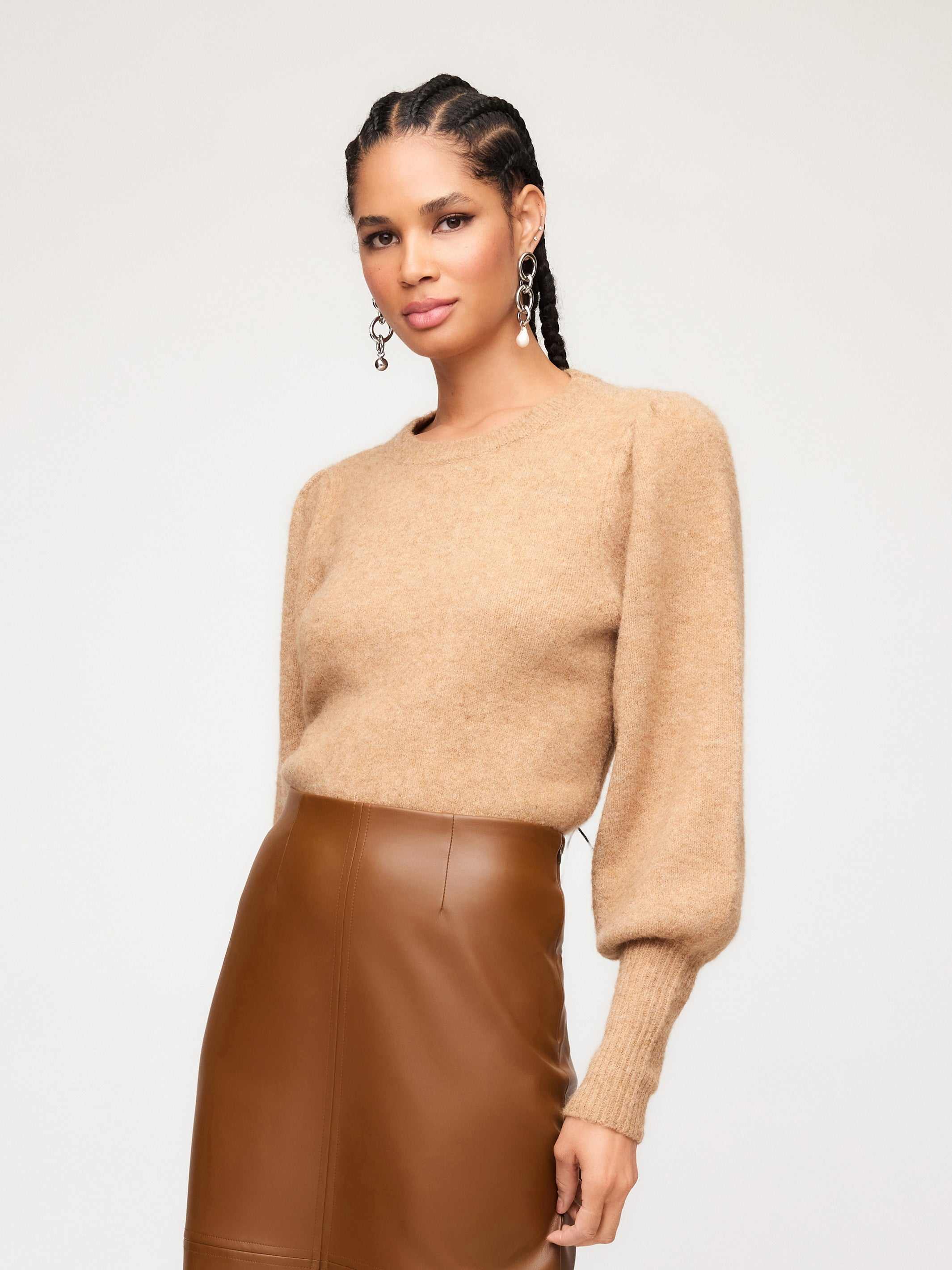 Woman wearing Lia Shirred Sleeve Sweater in camel color with long blouson sleeves and crew neck paired with brown leather skirt.