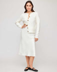 Woman wearing a white satin Mia Bias Skirt with an ivory button-up cardigan and black flats standing against a neutral background.