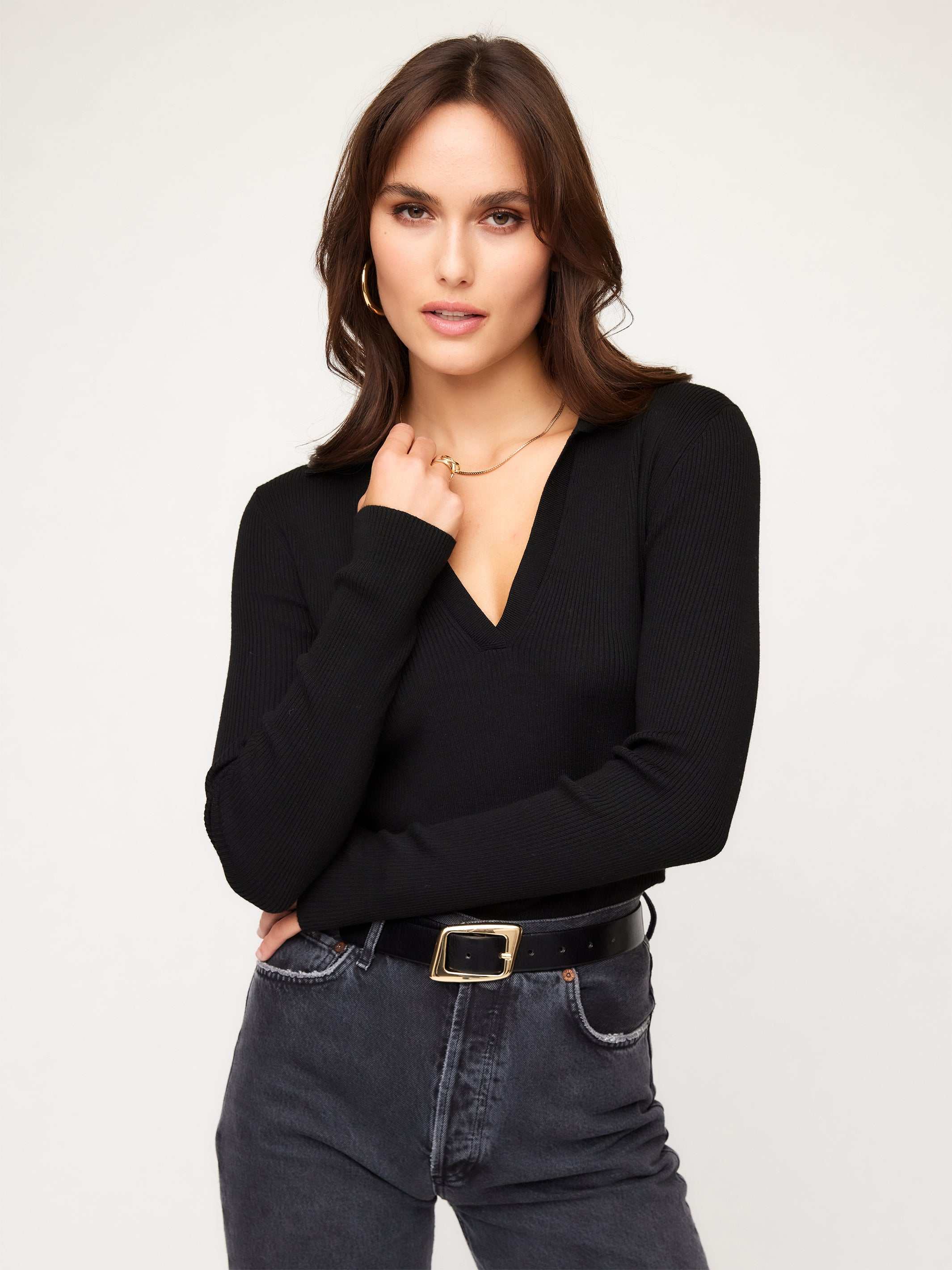 Woman wearing black Rory Sweater with V-neck and ribbed knit detail paired with jeans and black belt