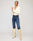 Woman wearing Rory Sweater, a cream ribbed knit cashmere blend V-neck sweater with collar, paired with blue jeans and cream knee-high boots.