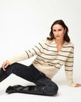 Woman wearing a cream Lisa Stripe Sweater with black stripes, collared V-neck, and ribbed cuffs, paired with black jeans and boots.