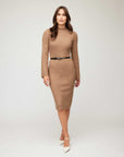 Beige fitted sweater dress with long flare sleeves and mock neck, styled with a black belt and white heels.