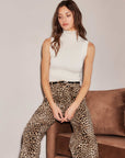 Woman wearing sleeveless Kelli Turtleneck Sweater paired with leopard print pants sitting on a brown couch