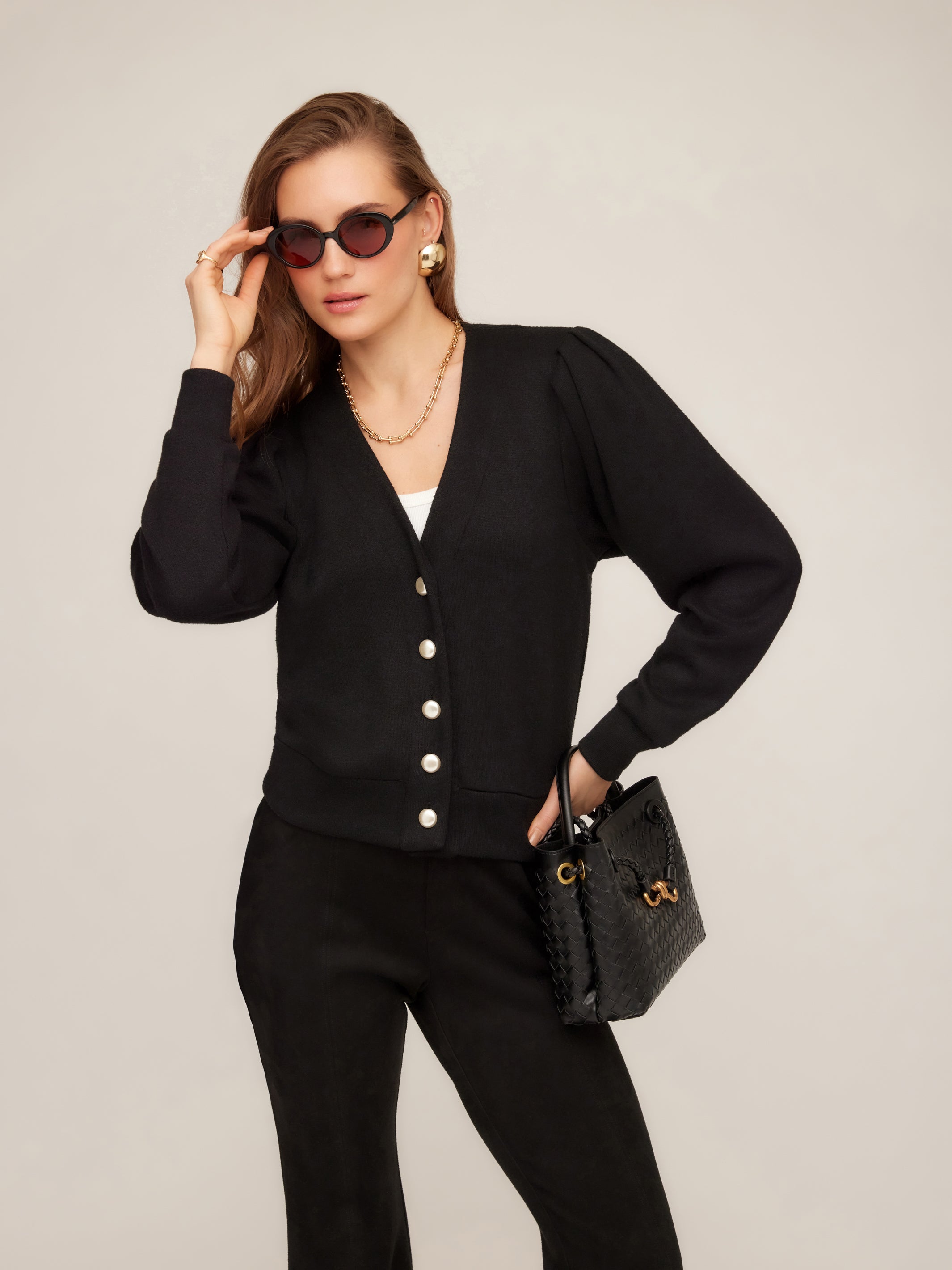 Woman wearing black Madeline Cardigan with V-neck, gathered shoulders, pearly buttons, and wide hem band.