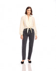 Woman wearing cream Capri tie-front blouse with V-neck and long blouson sleeves paired with black high-waisted jeans and black shoes