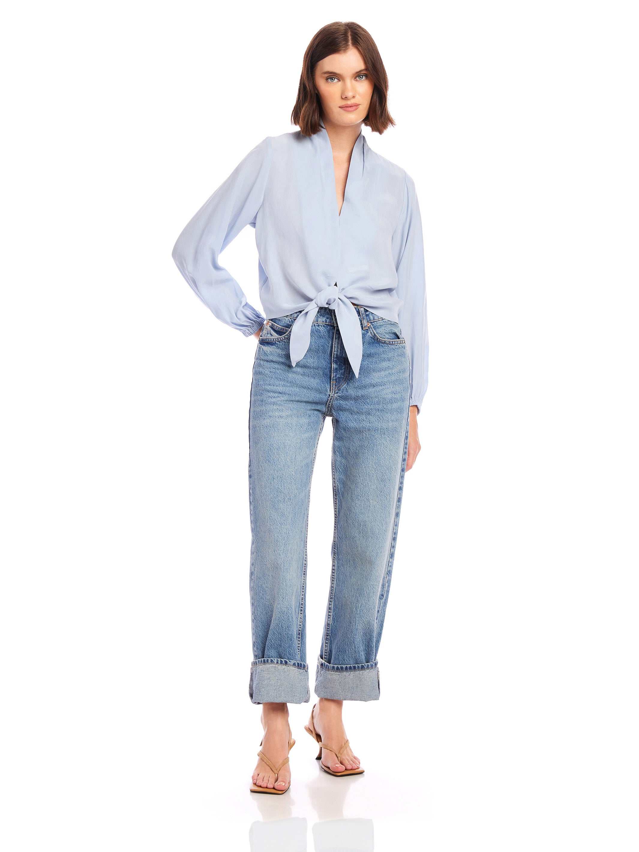 Woman wearing light blue Capri Tie-Front Blouse with long sleeves and V-neck paired with rolled-up jeans and sandals.