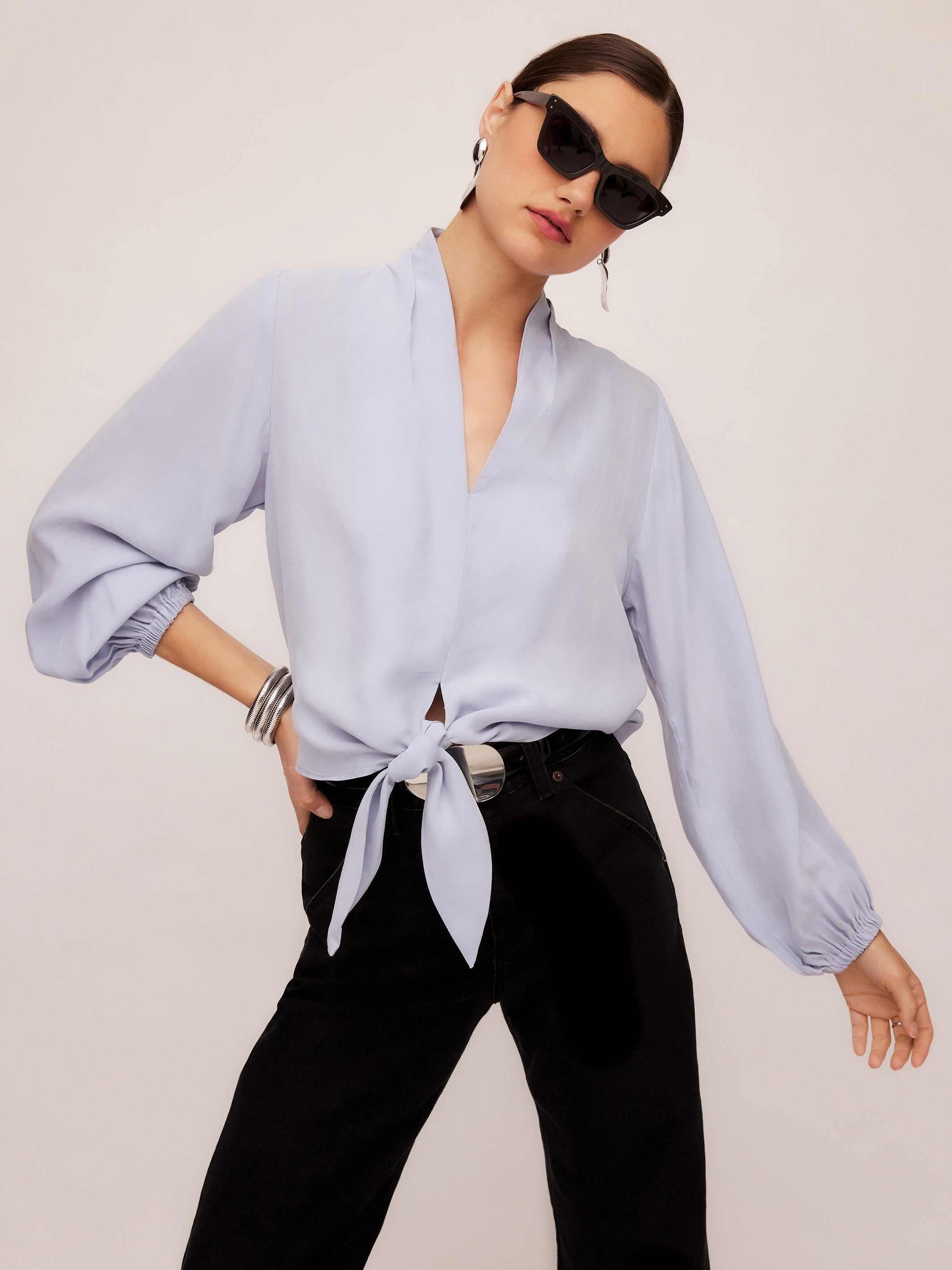 Woman wearing light blue Capri tie-front blouse with long blouson sleeves and black pants