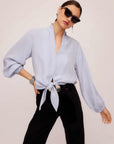 Woman wearing light blue Capri tie-front blouse with long blouson sleeves and black pants