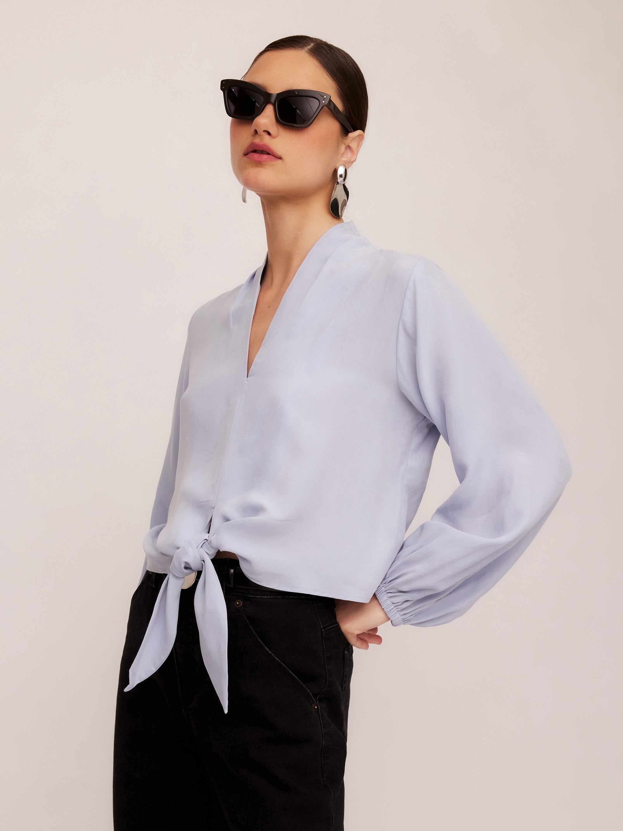 Woman wearing light blue Capri Tie-Front Blouse with long sleeves and elasticized cuffs paired with black pants and black sunglasses