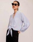 Woman wearing light blue Capri Tie-Front Blouse with long sleeves and elasticized cuffs paired with black pants and black sunglasses