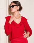 Woman wearing red Rita Ruffle Blouse with V-neck and front ruffle detail paired with gold accessories and sunglasses