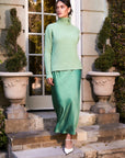 woman wearing green silky bias midi dress with green turtleneck sweater standing outdoors