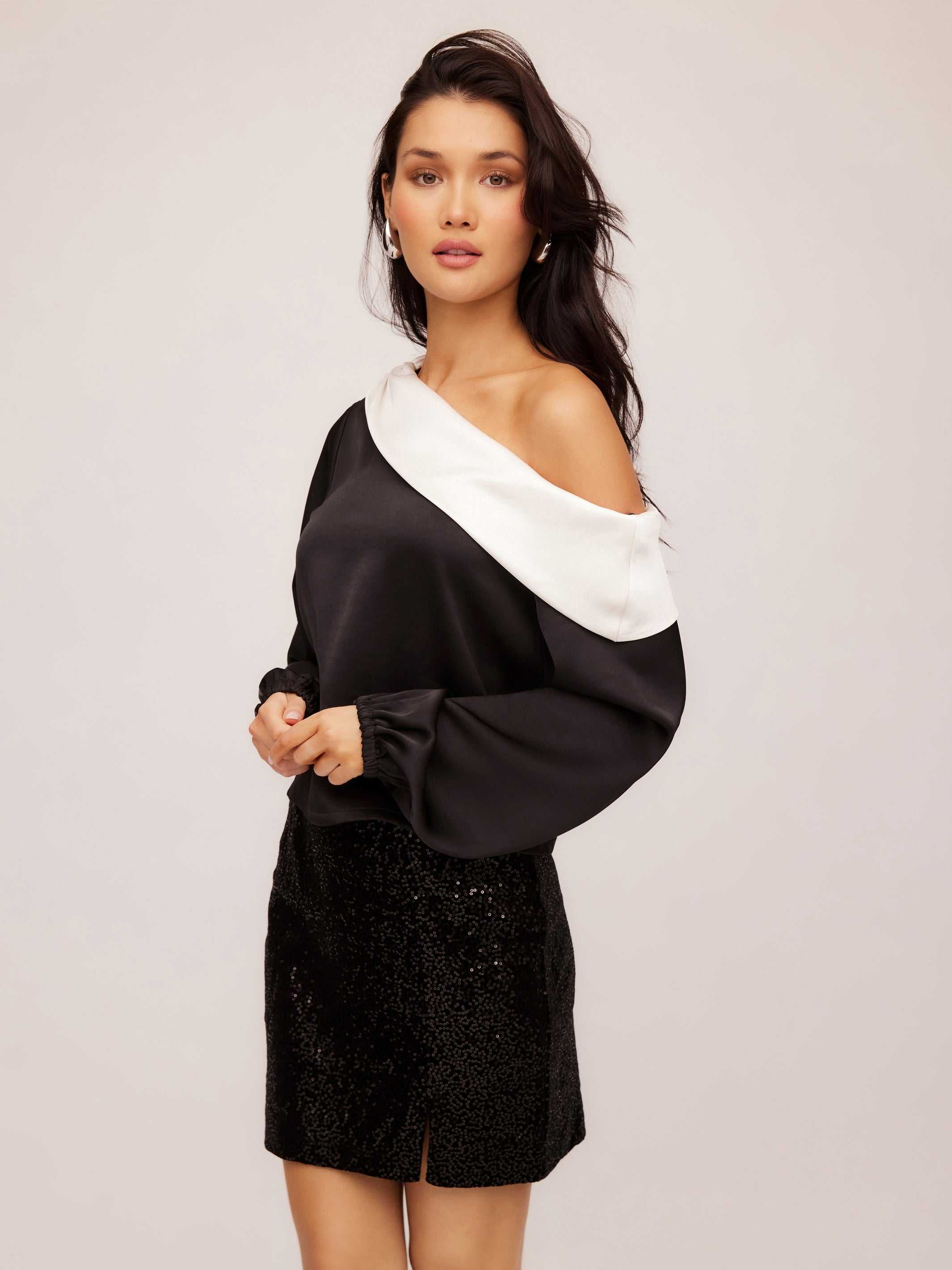 Woman wearing Marisa One-Shoulder Top in black and white satin with long blouson sleeves and elasticized cuffs.