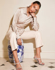 Woman wearing a silky satin Tawnie Side-Pleat Shirt with cuffed sleeves and button-down collar, styled with light trousers and heels