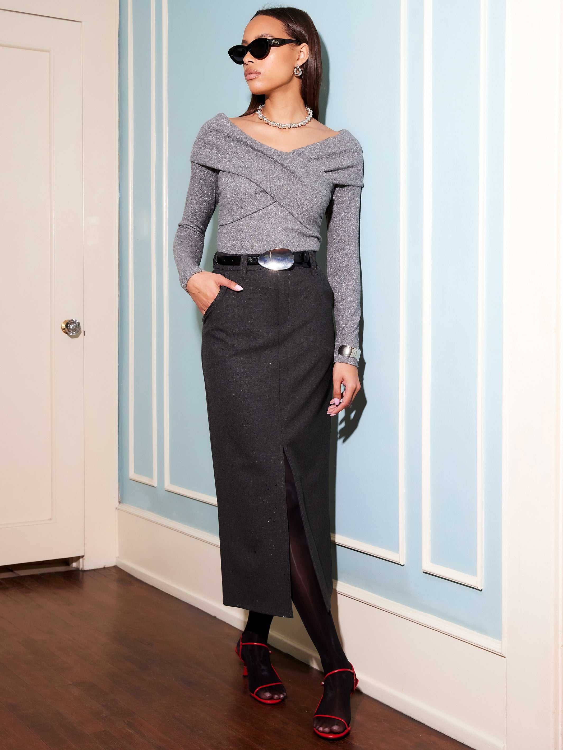 Woman wearing Claire Skirt, a black pencil skirt with front slit, styled with a grey off-shoulder top and black belt.