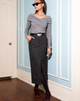 Woman wearing Claire Skirt, a black pencil skirt with front slit, styled with a grey off-shoulder top and black belt.