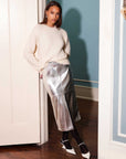 Woman wearing silver Kaia faux leather midi skirt with front slit and white sweater indoors
