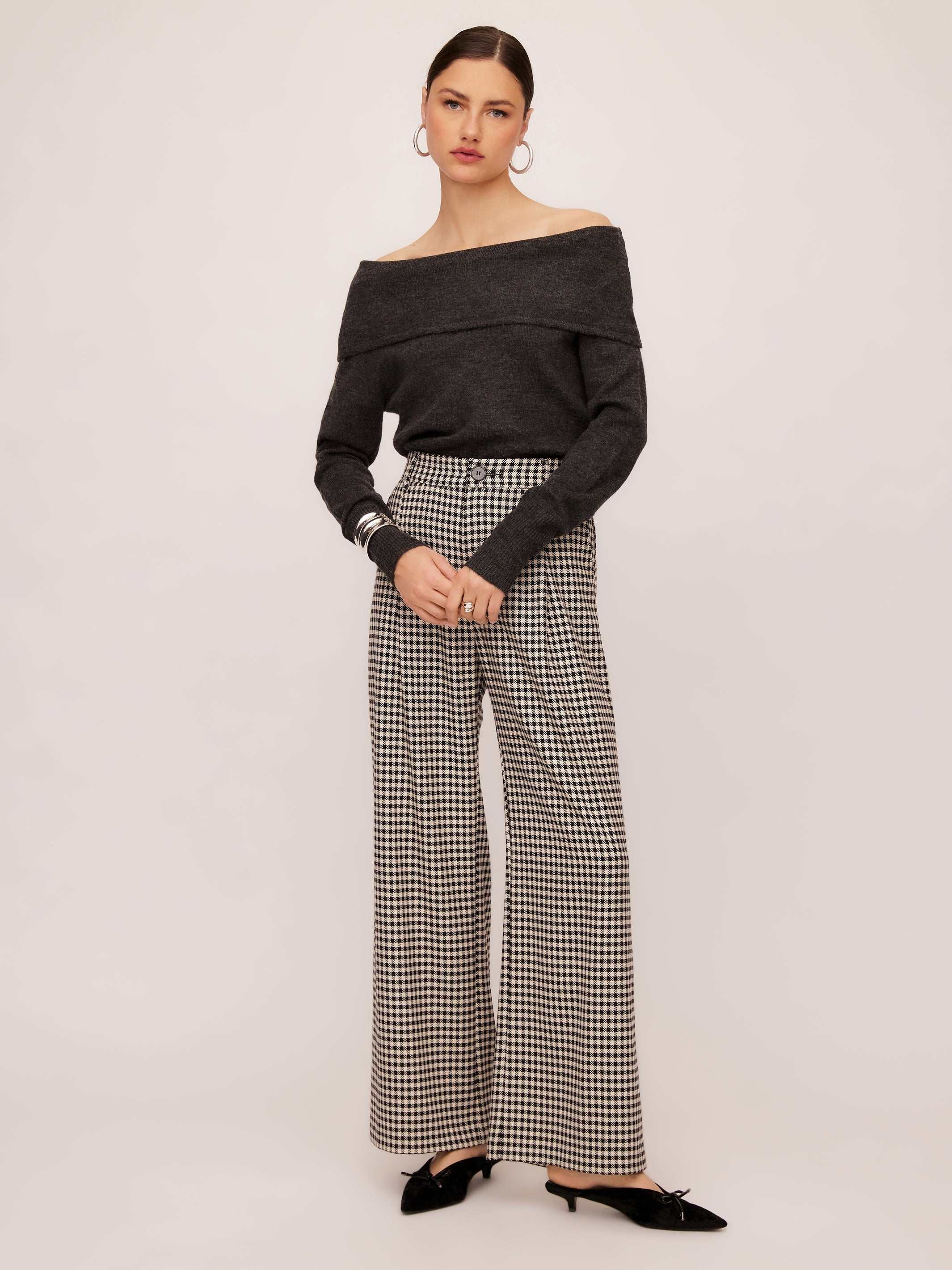 Woman wearing Mina Pants with herringbone check pattern and wide leg silhouette paired with off-shoulder dark gray top and black shoes