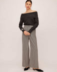 Woman wearing Mina Pants with herringbone check pattern and wide leg silhouette paired with off-shoulder dark gray top and black shoes