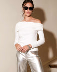 Woman wearing white asymmetric one-shoulder long sleeve top with fold-over neck and silver pants
