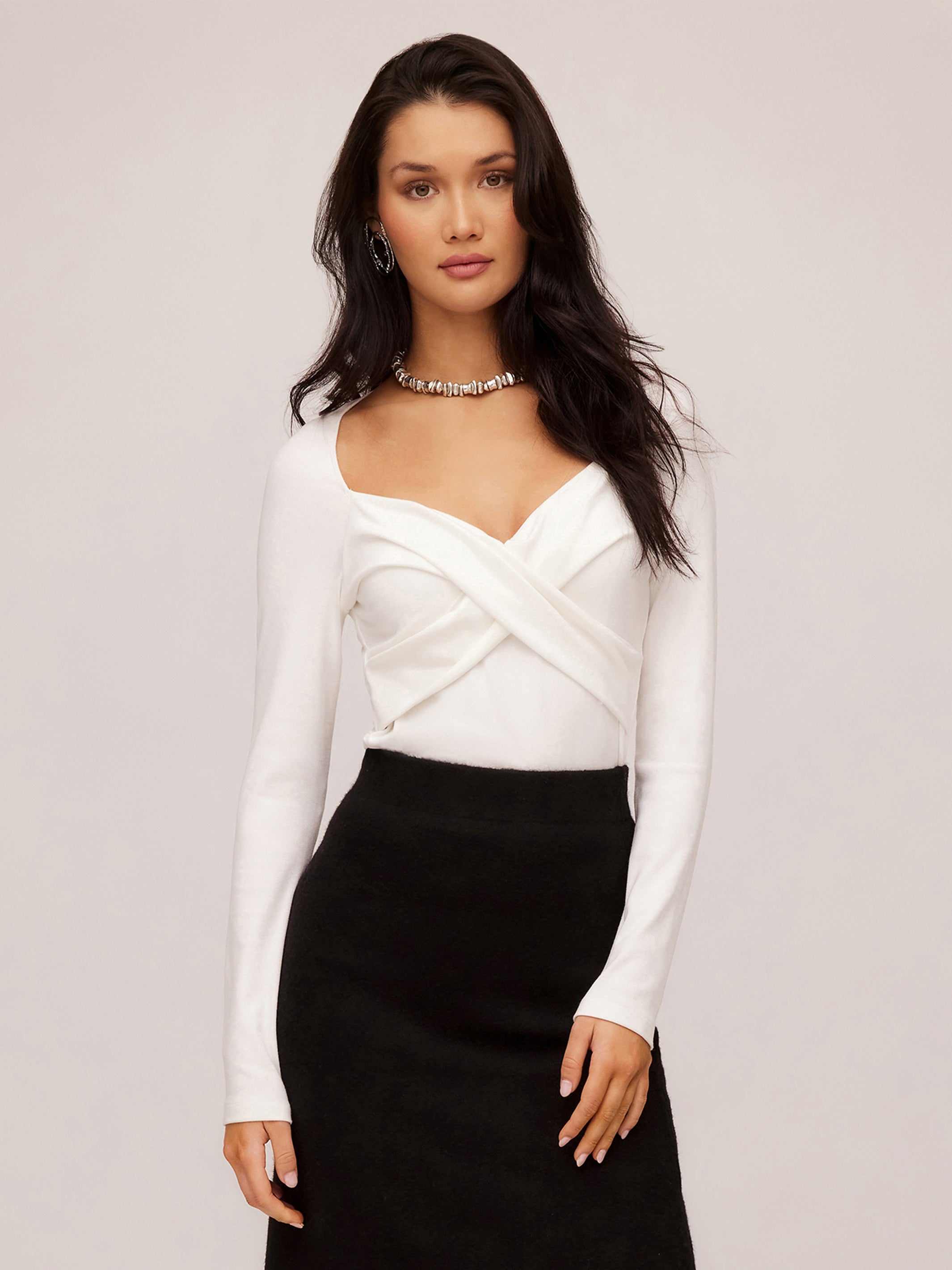 Woman wearing white Zelda Crossover Top with long sleeves and sweetheart neckline paired with black skirt
