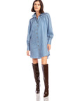 Woman wearing a light blue chambray stripe Natalia Shirtdress with long peasant sleeves and button front paired with knee-high brown boots.