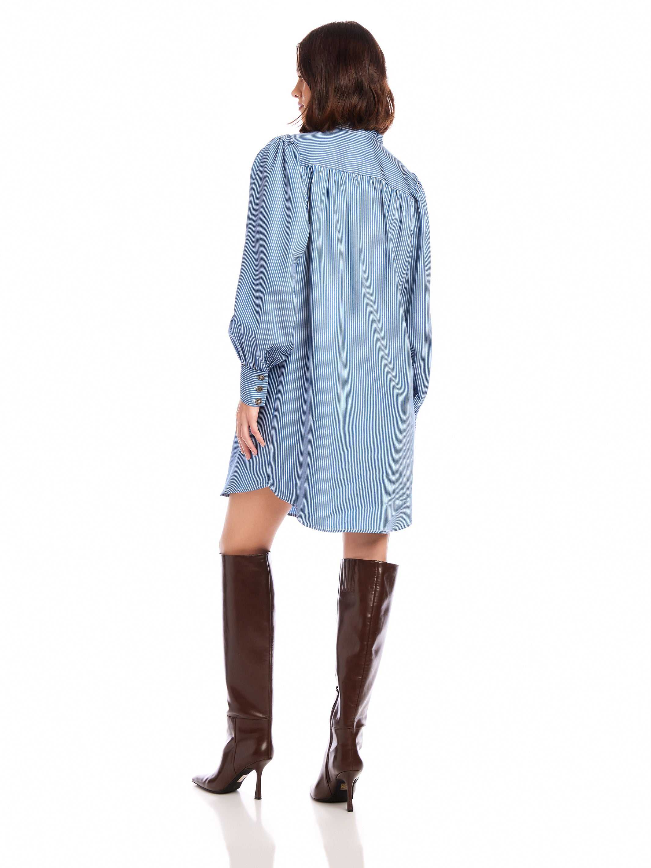 Back view of a woman wearing a light blue Natalia Shirtdress with long peasant sleeves and button cuffs paired with brown thigh high boots