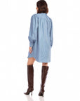 Back view of a woman wearing a light blue Natalia Shirtdress with long peasant sleeves and button cuffs paired with brown thigh high boots