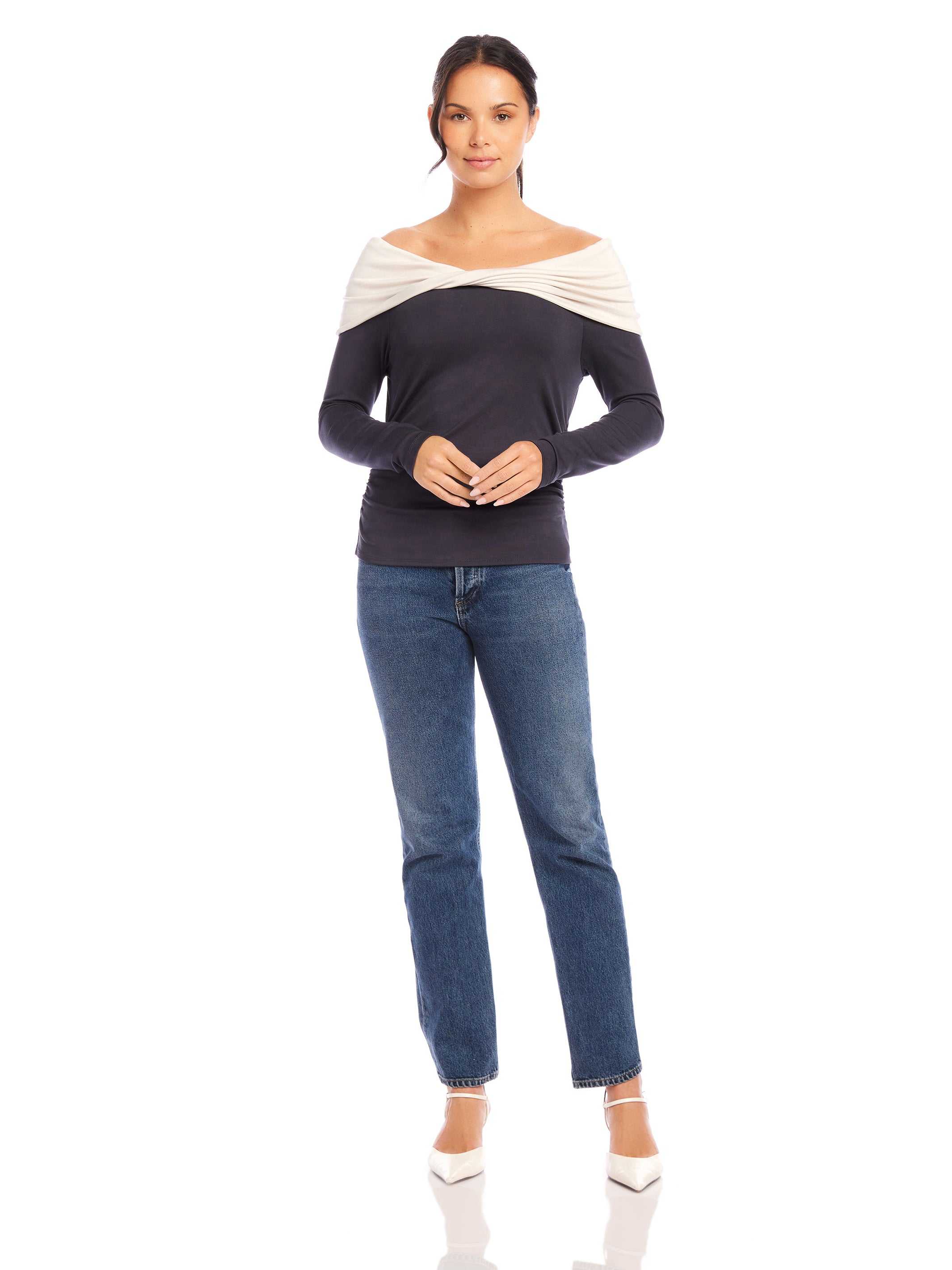 Woman wearing Jillian Off-The-Shoulder Top with twist neck and side shirring in black and cream color, paired with blue jeans and white heels