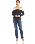 Woman wearing Jillian Off-The-Shoulder Top with twist neck and side shirring in black and cream color, paired with blue jeans and white heels