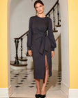 Woman wearing black Addie Side-Knot midi dress with long sleeves and side slit standing indoors