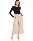 Woman wearing beige wide-leg cropped Sadie Trousers made of pinstripe linen with front pleats and side pockets paired with a black long-sleeve top.
