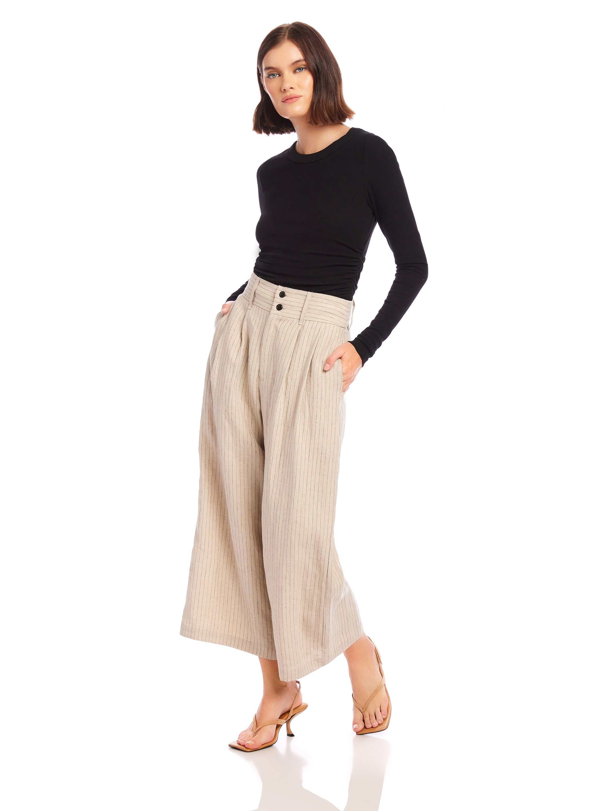 Woman wearing beige pinstripe linen Sadie Trousers with wide leg and cropped length paired with black long-sleeve top