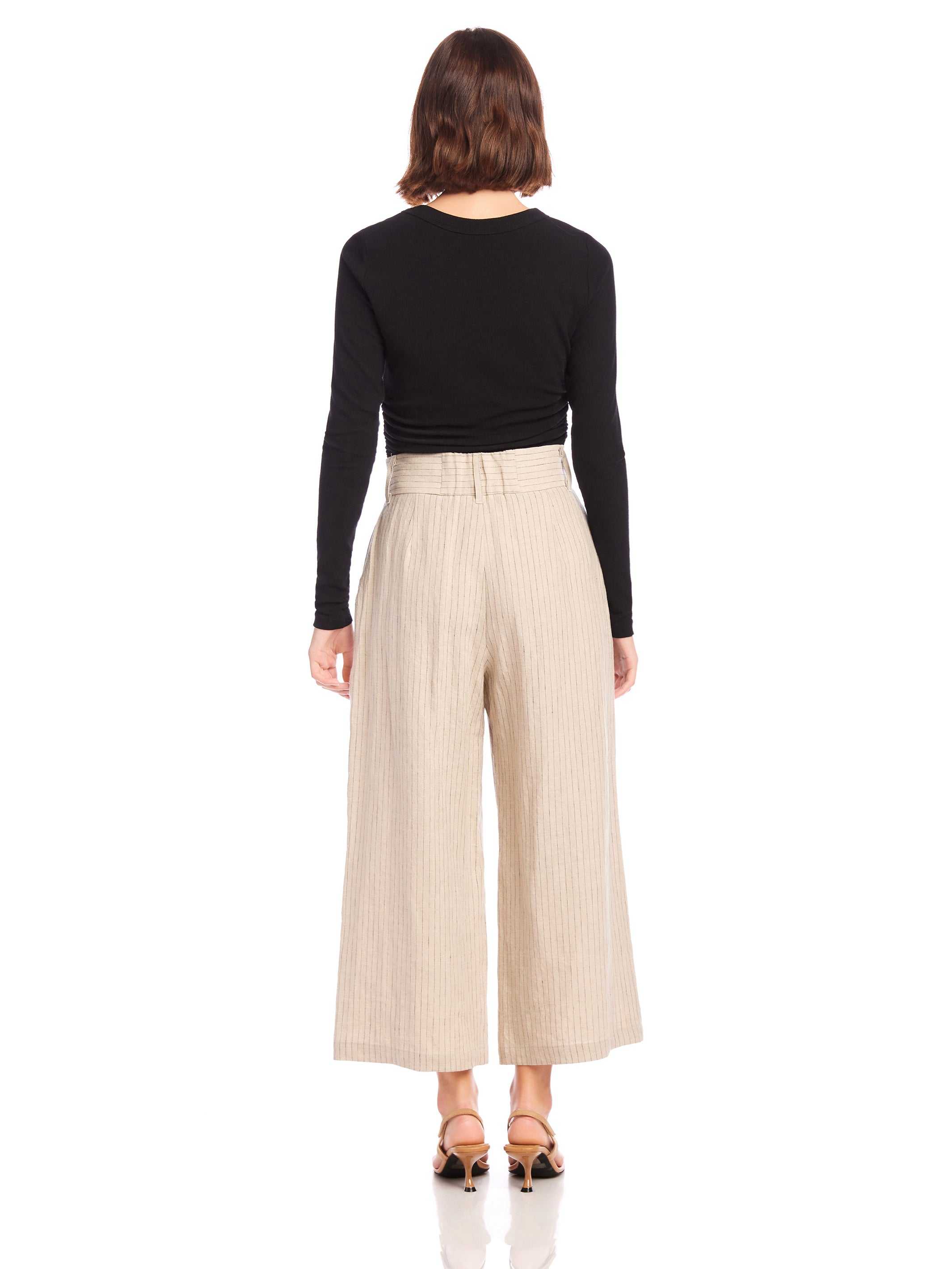 Woman wearing beige pinstripe linen Sadie Trousers with wide leg and cropped length, paired with black long-sleeve top.