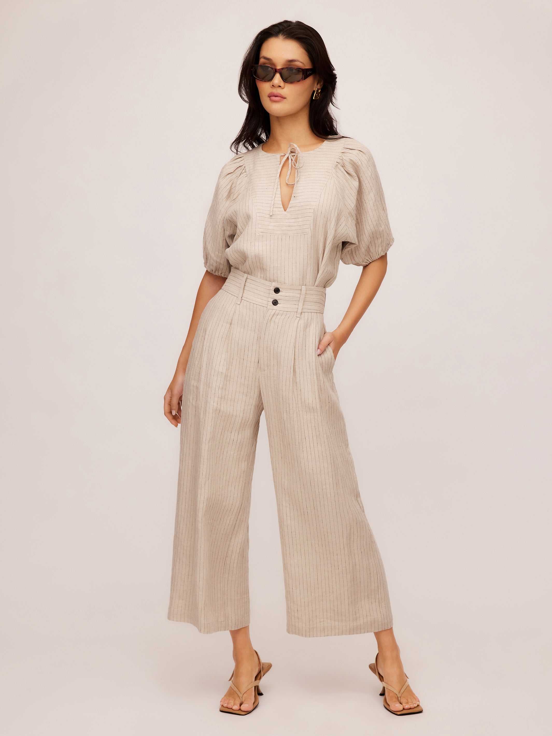 Woman wearing beige pinstripe linen Sadie Trousers with wide leg cropped style and front pleats.