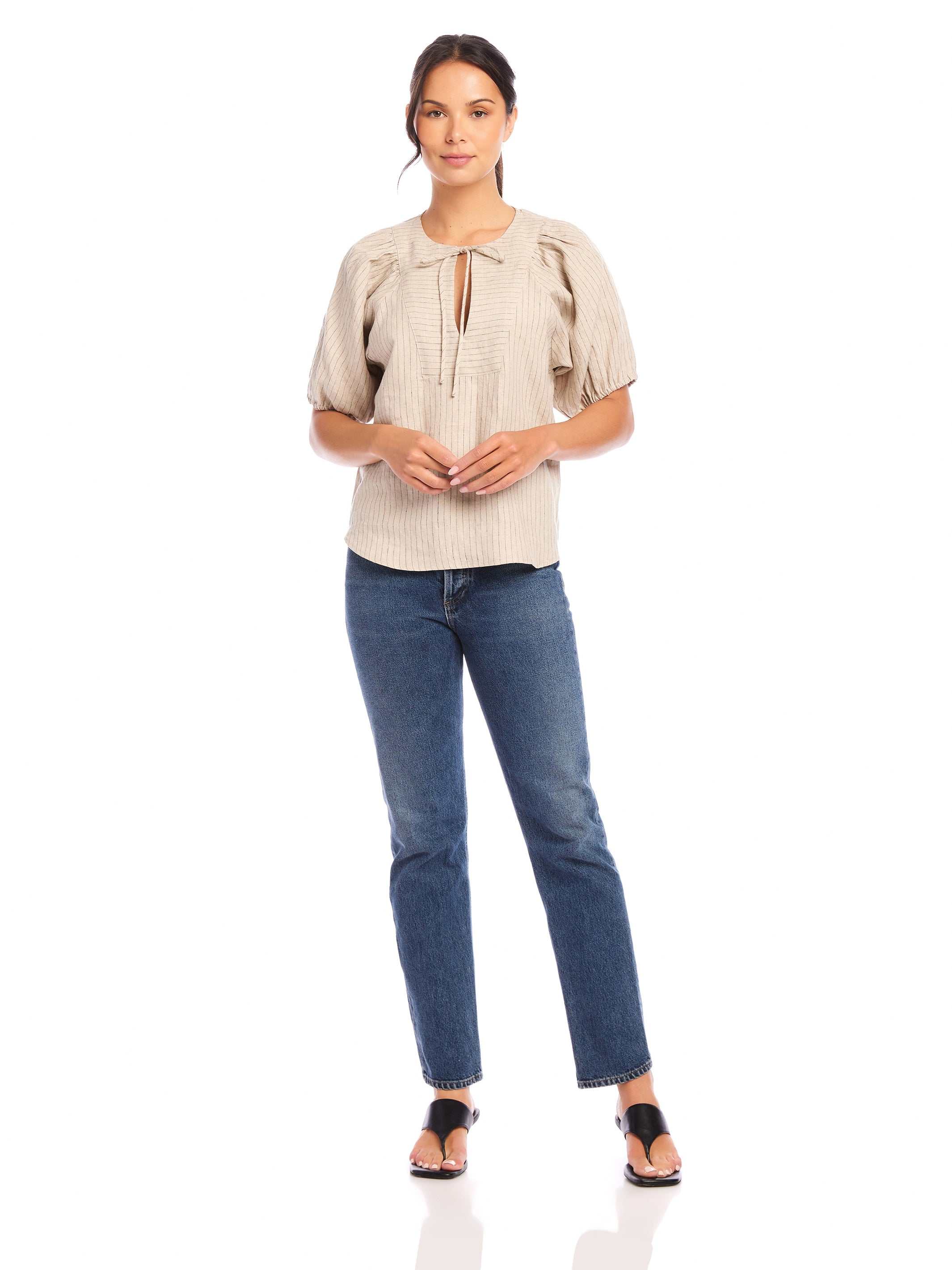Woman wearing beige Imogen Poof Sleeve Top with short poof sleeves and split neck, paired with blue jeans and black sandals.