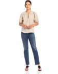 Woman wearing beige Imogen Poof Sleeve Top with short poof sleeves and split neck, paired with blue jeans and black sandals.
