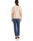 Woman wearing beige pinstripe linen Imogen Poof Sleeve Top with short elasticized poof sleeves and split neck tie, paired with blue jeans, back view.