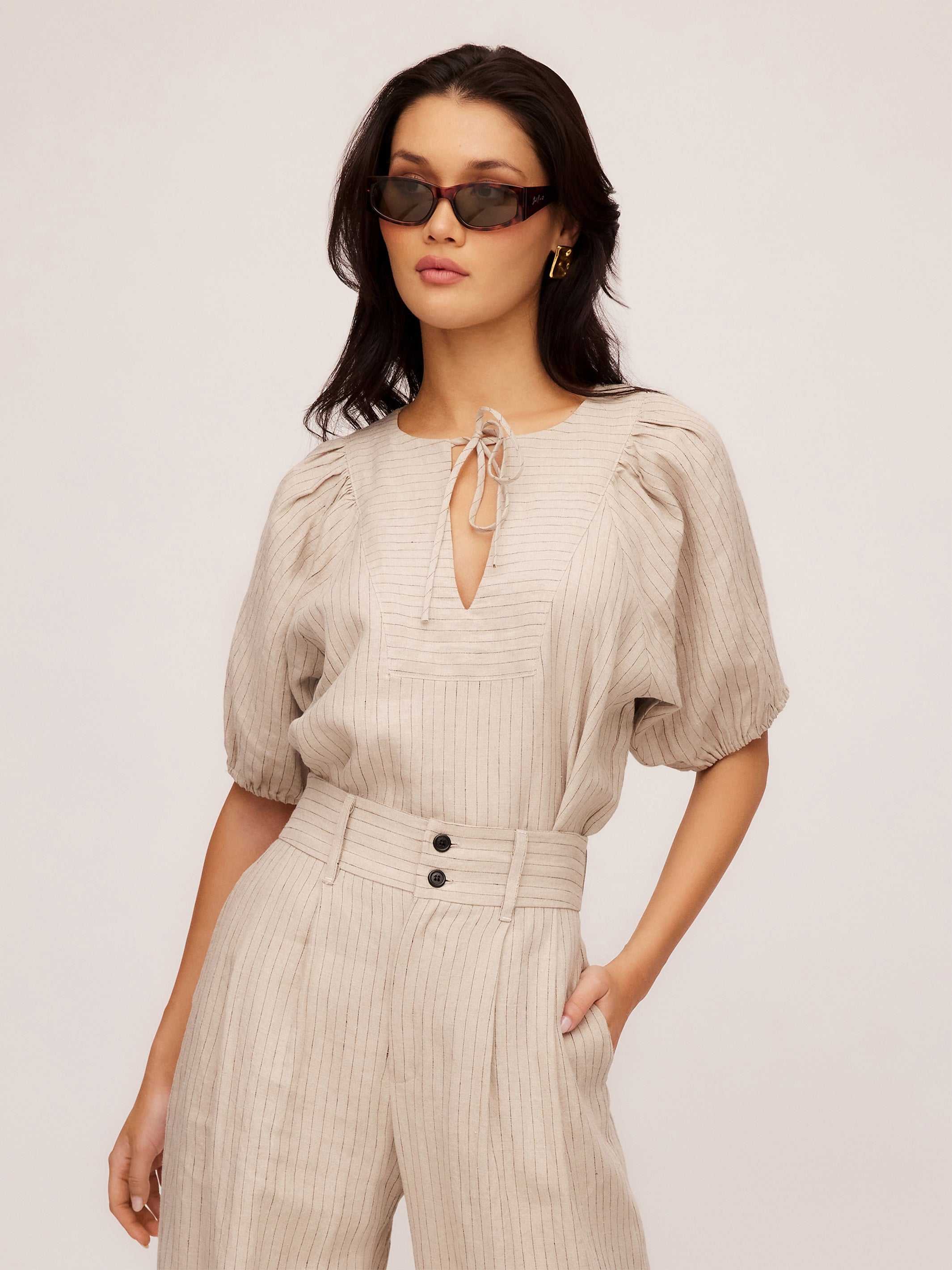 Woman wearing beige Imogen Poof Sleeve Top with pinstripe linen and matching high-waist trousers