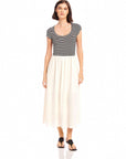 Woman wearing Contrast Hem Sylvie Dress with black and white striped jersey top and solid cream skirt, short cap sleeves, and side pockets.