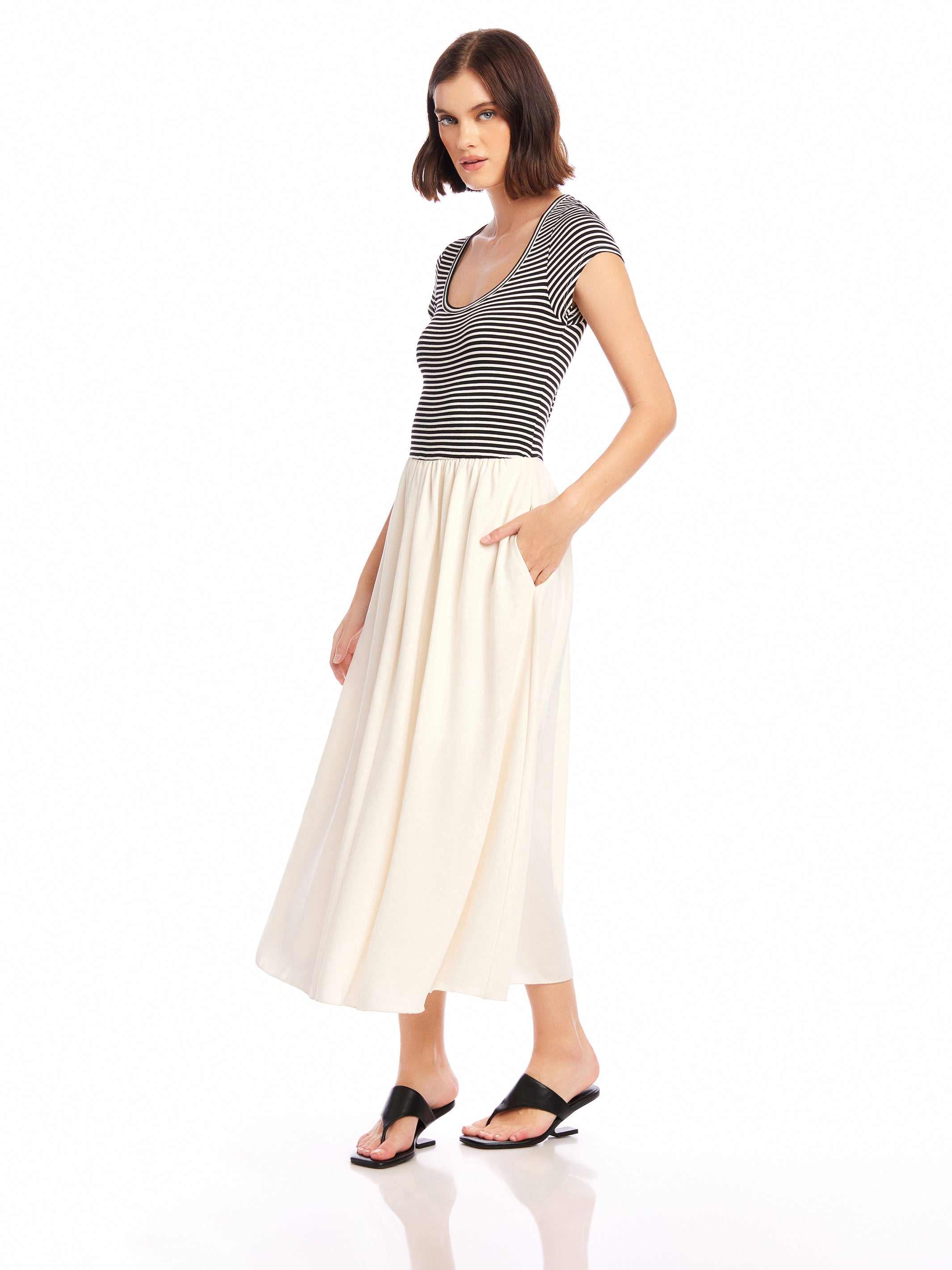Woman wearing a Contrast Hem Sylvie Dress with a striped black and white jersey top and a contrasting cream skirt with side pockets and short cap sleeves.