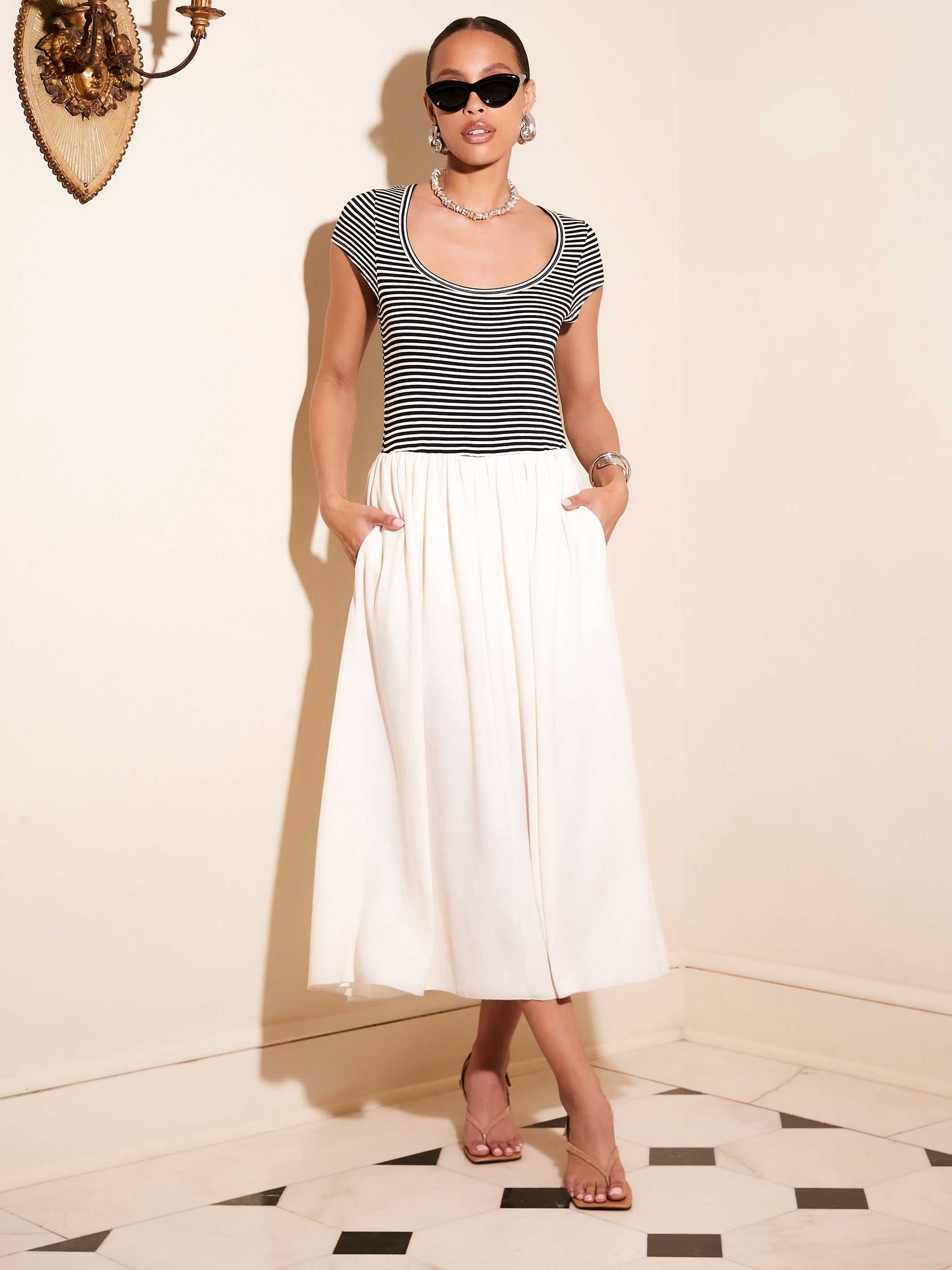 Woman wearing Contrast Hem Sylvie Dress with black and white striped jersey top and white skirt, posing indoors with sunglasses and sandals.