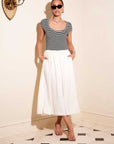 Woman wearing Contrast Hem Sylvie Dress with black and white striped jersey top and white skirt, posing indoors with sunglasses and sandals.