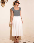 Contrast Hem Sylvie Dress with black striped jersey top and white skirt, short sleeves, scoop neck, side pockets, styled with sunglasses and earrings.