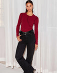 Woman wearing brick red Elissa Long Sleeve Tee with exposed seam detail and slim fit paired with black jeans