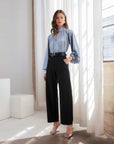 Woman wearing blue Alana Keyhole Top with knotted neckline and black wide-leg trousers in bright room